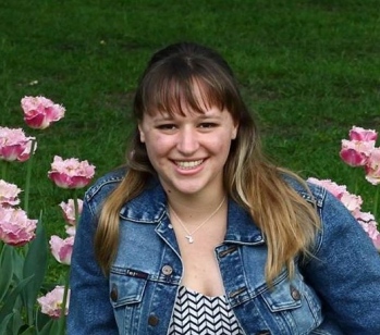 Katie smiling in a garden with flowers behind her
