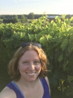 Denise smiling in front of grapevines