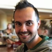 Image of Vaughn looking into the camera with a big smile. His dark hair is slightly peaked in the middle and he has short facial hair.